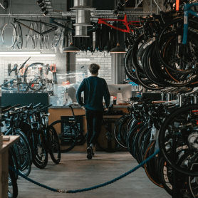 Ein Mann in einer Fahrradwerkstatt voller aufgehängter Fahrräder, die auf ihre Reparatur warten.